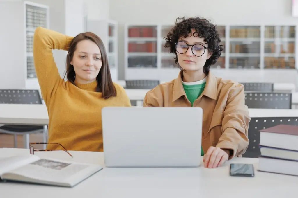 two female colleagues work on laptops in coworking office, library. online training webinar